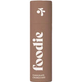 A brown cylindrical tube labeled "Foodie Chocolate Crunch Kiss Lip Balm 10g" stands upright against a white background—this chocolate lip balm features plastic-free packaging.