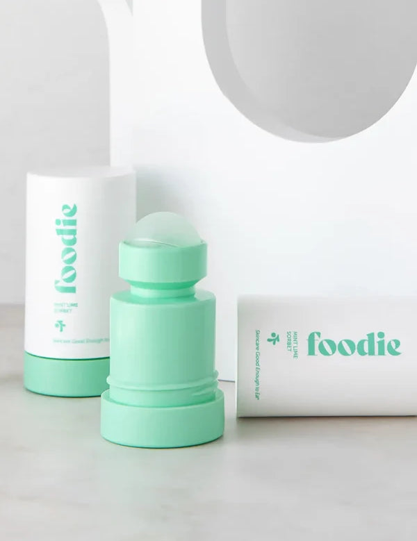 Mint-green Foodie Mint Lime Sorbet roll-on deodorant with its rounded roller ball exposed, standing beside white outer covers on a curved white display.