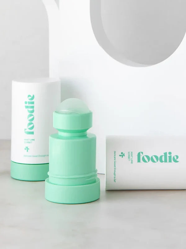 Mint-green Foodie Mint Lime Sorbet roll-on deodorant with its rounded roller ball exposed, standing beside white outer covers on a curved white display.