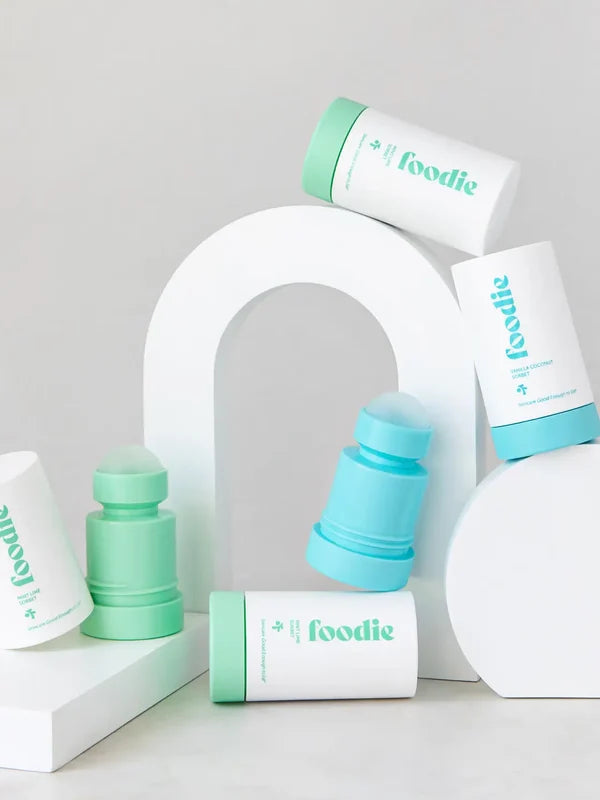 Foodie roll-on deodorants in mint green and turquoise, with rounded roller balls exposed, arranged among white outer covers and curved white display blocks.