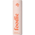 A light pink cylindrical bottle of Foodie Tropical Pavlova Pout Lip Balm 10g features large orange "foodie" lettering with "TROPICAL PAVLOVA POUT" below, both vertically aligned. The cap has an orange abstract design and is plastic-free.