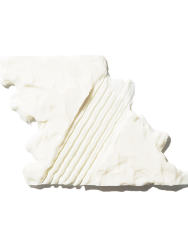 A thick white swatch of 100% Pure Glossy Locks Glossing Conditioner, spread into an irregular rectangle with closely spaced grooves through the centre.