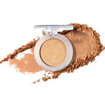 A single open compact of 100% Pure Fruit Pigmented® Eye Shadow 2g by 100% Pure in shimmery gold, with loose powder smeared around it on a white background.