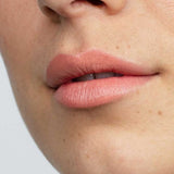 Close-up of lips in a matte, natural pink from Antipodes Moisture Boost Natural Lipsticks 4g. Skin looks smooth with freckles and light texture. "Golden Bay Nectar" at the bottom highlights long-lasting, natural color.