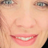 Close-up of a woman with blue eyes, long lashes, and pink lips. Her fair skin and dark hair frame her face. "Guava Blush" from Luk Beautifood Lip Nourish Lipsticks 3g, made with food-grade ingredients, is highlighted at the bottom.