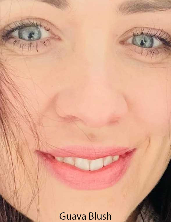 Close-up of a woman with blue eyes, long lashes, and pink lips. Her fair skin and dark hair frame her face. "Guava Blush" from Luk Beautifood Lip Nourish Lipsticks 3g, made with food-grade ingredients, is highlighted at the bottom.