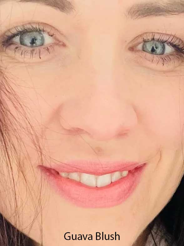 Close-up of a woman with blue eyes, long lashes, and pink lips. Her fair skin and dark hair frame her face. "Guava Blush" from Luk Beautifood Lip Nourish Lipsticks 3g, made with food-grade ingredients, is highlighted at the bottom.