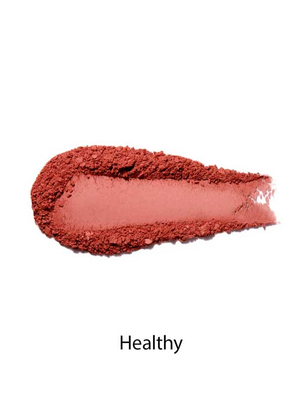 A swatch of 100% Pure Rice Powder Pressed Blush 9g in matte, dusty pink on a white background with "Healthy" below, demonstrating a natural flush and buildable coverage.