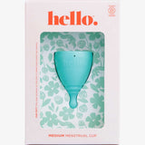 The Hello Period Cup Medium is a teal menstrual cup made from medical-grade TPE, in floral packaging labeled "hello." and "MEDIUM MENSTRUAL CUP," displayed in a white and pink box with a clear window showing the reusable period cup inside.