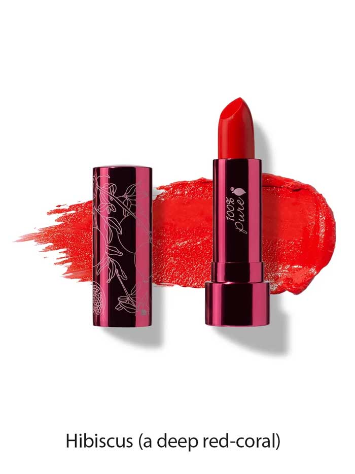 A tube of 100% Pure Pomegranate Oil Moisturising Lipstick 4.5g (vegan, deep red-coral) sits uncapped on a matching swatch. The label reads Hibiscus—a hydrating formula for bold, vibrant lips.