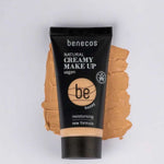 A tube of Benecos Natural Creamy Makeup 30ml in honey sits on a matching foundation smear. The packaging highlights its vegan, moisturising formula and new formula against a light background.