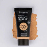 A tube of Benecos Natural Creamy Makeup 30ml in honey sits on a matching foundation smear. The packaging highlights its vegan, moisturising formula and new formula against a light background.
