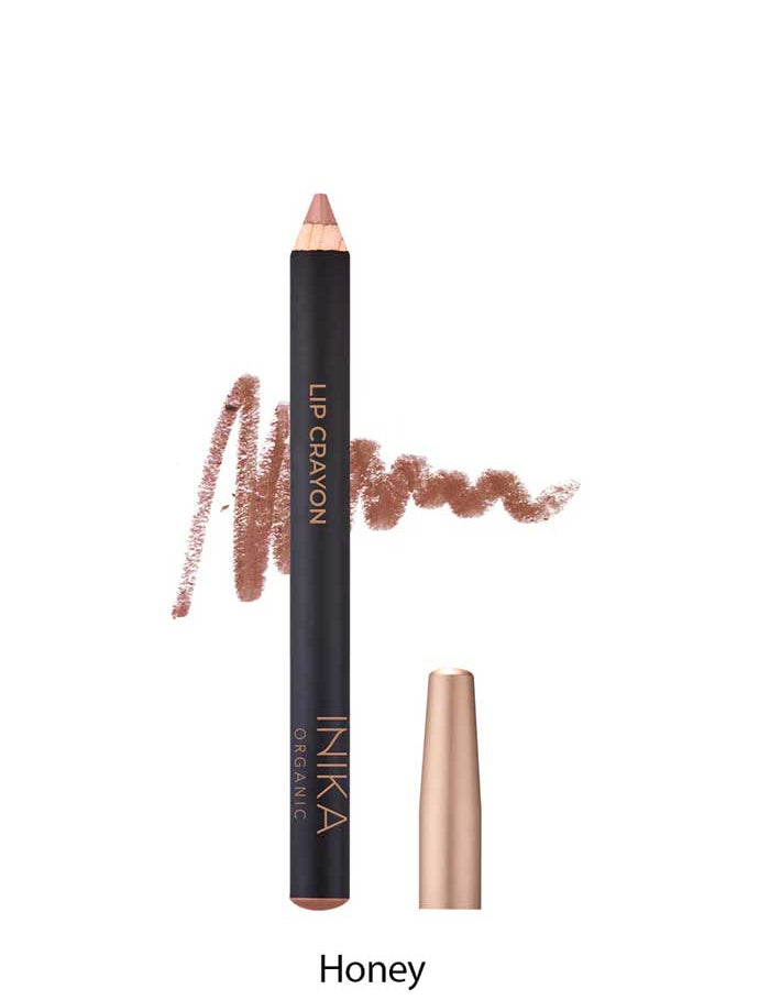 A brown INIKA Organic Lip Crayon 6.7g with gold labeling is displayed with its cap removed and a swatch behind it; the shade "Honey" is shown below, emphasizing this long-lasting lip liner’s natural, organic appeal.