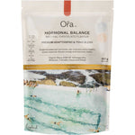 A white pouch of Ora Hormonal Balance Powder Chocolate 300g highlights its adaptogenic blend for PMS support. The lower part features an aerial shot of people swimming in a turquoise sea.