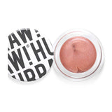 Hurraw! Copper Aura Balm 5.8g is a vegan, shimmery rose-gold cream highlighter in a round container. The white lid, featuring bold black text in a playful, overlapping style, is off and placed to the left of the open balm.