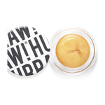 An open round container of Hurraw! Gold Aura Balm 5.8g, a vegan gold cream highlighter with a shimmery finish. The white lid, displaying bold black text "RAW! HU", sits slightly askew beside the product.