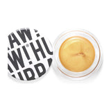 An open round container of Hurraw! Gold Aura Balm 5.8g, a vegan gold cream highlighter with a shimmery finish. The white lid, displaying bold black text "RAW! HU", sits slightly askew beside the product.
