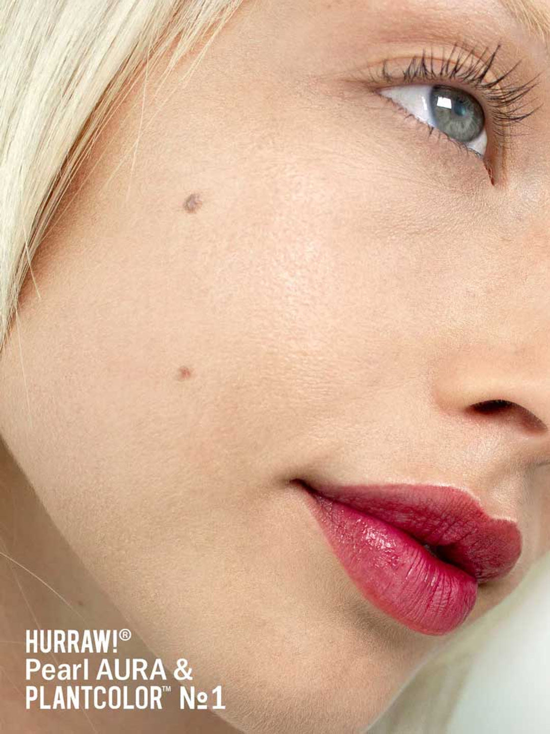 A close-up of a fair-skinned, blonde, blue-eyed person with a beauty mark. They wear bold rose lipstick and a hint of Hurraw! Pearl Aura Balm 5.8g. Text: Hurraw! Pearl Aura Balm 5.8g & PLANTCOLOR №1.