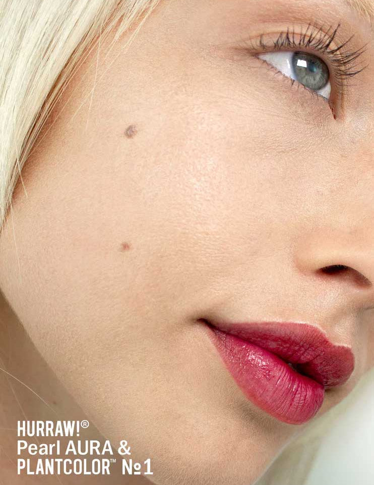 A close-up of a fair-skinned, blonde, blue-eyed person with a beauty mark. They wear bold rose lipstick and a hint of Hurraw! Pearl Aura Balm 5.8g. Text: Hurraw! Pearl Aura Balm 5.8g & PLANTCOLOR №1.