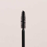 A close-up of the INIKA Organic Bold Lash Mascara Black 13ml wand, its bristles coated in black mascara, is shown vertically against a plain light beige background.