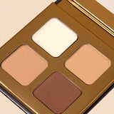 A close-up of the INIKA Organic Brow Palette 8g, an open vegan set with four shades—off-white, light beige, medium tan, and deep brown—in a gold case against a light background.