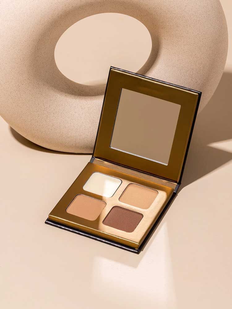 The INIKA Organic Brow Palette 8g, an open vegan palette with four neutral shades and a mirror, is shown on a beige surface next to a round, textured decor object—ideal for creating versatile brow looks.