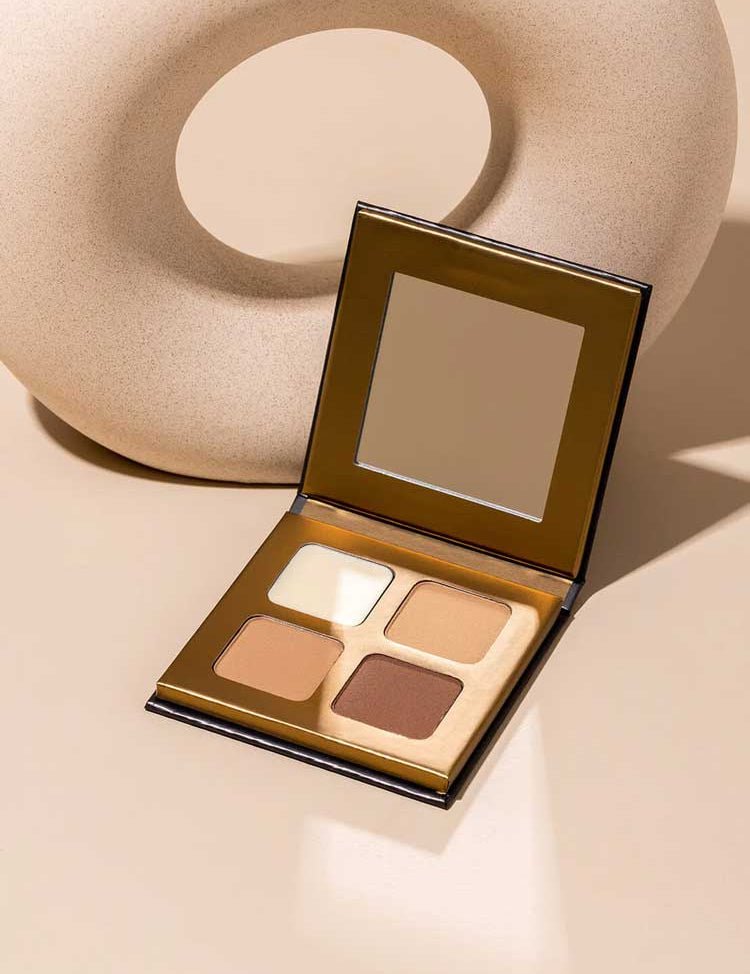 The INIKA Organic Brow Palette 8g, an open vegan palette with four neutral shades and a mirror, is shown on a beige surface next to a round, textured decor object—ideal for creating versatile brow looks.