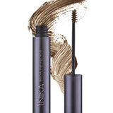 A tube of INIKA Organic Brow Perfector 6.5ml in Walnut stands open with its brush visible, set against a background of a natural eyebrow gel smear.