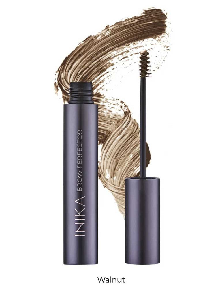 A tube of INIKA Organic Brow Perfector 6.5ml in Walnut stands open with its brush visible, set against a background of a natural eyebrow gel smear.