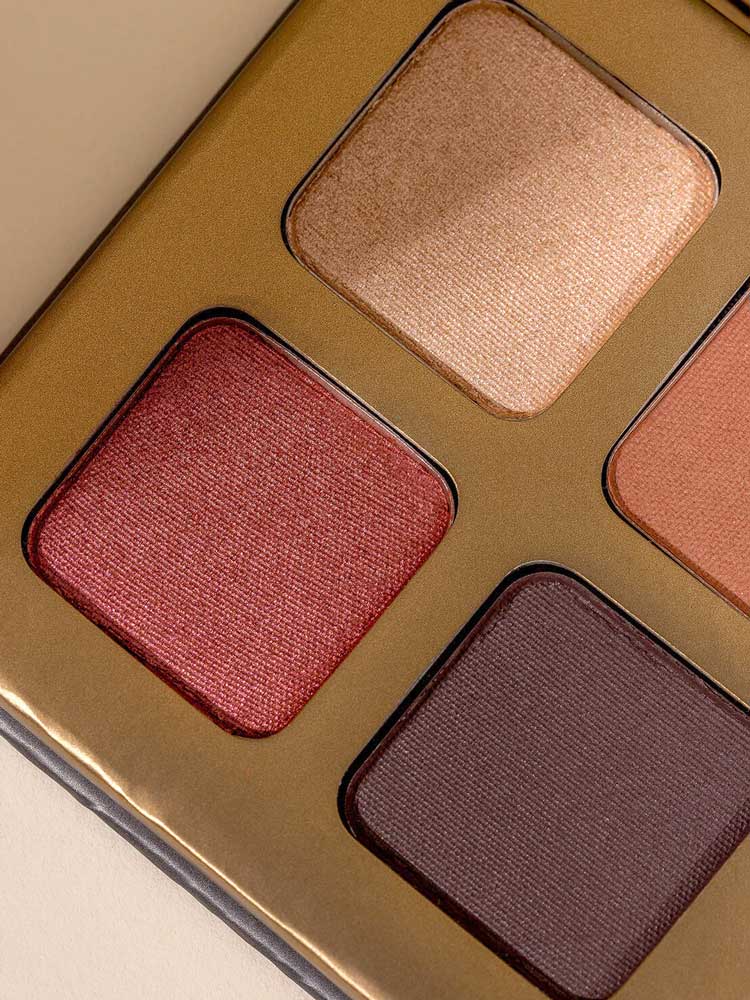 Close-up of the INIKA Organic Eyeshadow Quad - Flowers 8g, featuring four shimmery mineral shades—gold, rose, brown, and dark plum—arranged in a sleek gold-colored rectangular case.