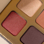 Close-up of the INIKA Organic Eyeshadow Quad - Flowers 8g, featuring four shimmery mineral shades—gold, rose, brown, and dark plum—arranged in a sleek gold-colored rectangular case.
