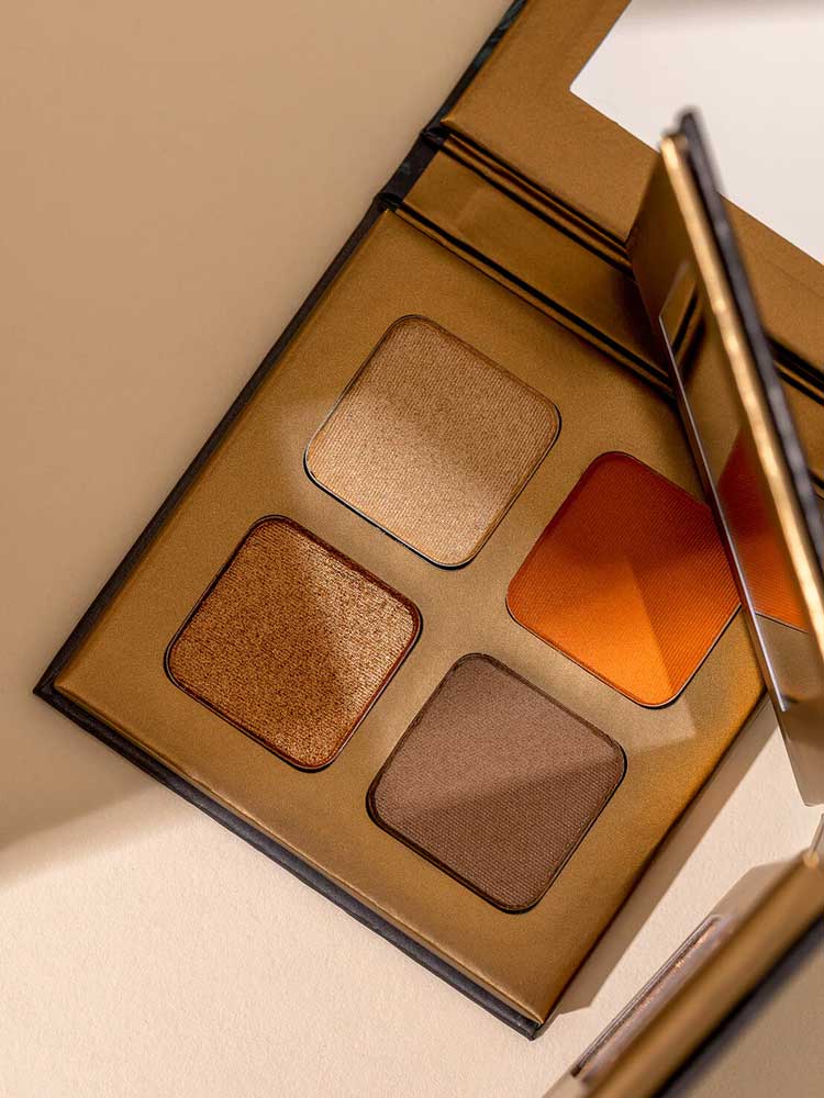 The INIKA Organic Eyeshadow Quad - Sunset 8g features four talc-free shades—gold, orange, bronze, and brown—in a gold mirrored case. Photographed on a light beige surface.