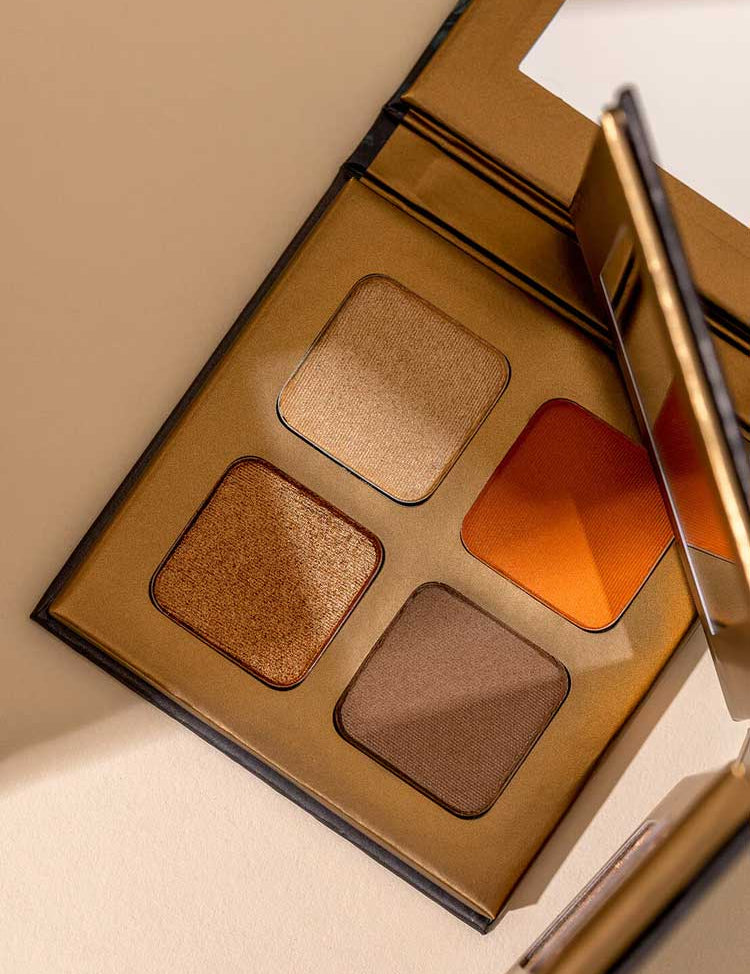 The INIKA Organic Eyeshadow Quad - Sunset 8g features four talc-free shades—gold, orange, bronze, and brown—in a gold mirrored case. Photographed on a light beige surface.
