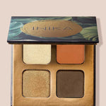 An open INIKA Organic Eyeshadow Quad - Sunset 8g shows four shades—shimmery gold, matte orange, shimmery bronze, and matte brown—in a decorative case with a green and gold lid design.