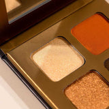 Close-up of the INIKA Organic Eyeshadow Quad - Sunset 8g, a natural palette with a mirror, featuring shimmery gold, bronze, and matte orange mineral shades in a sleek metallic gold case.