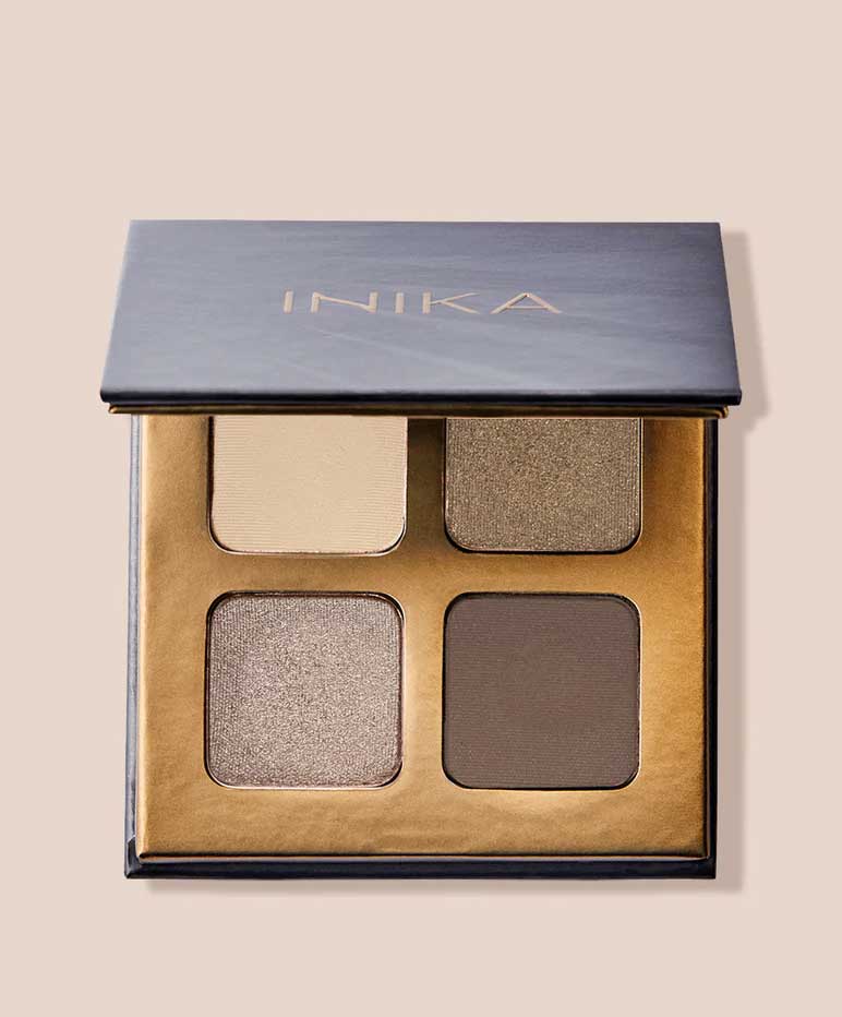 The INIKA Organic Eyeshadow Quad - Wind 8g is a vegan, talc-free palette in a black and gold case, featuring four neutral shades—beige, taupe, shimmery champagne, and matte brown. The lid displays "INIKA" in gold lettering.