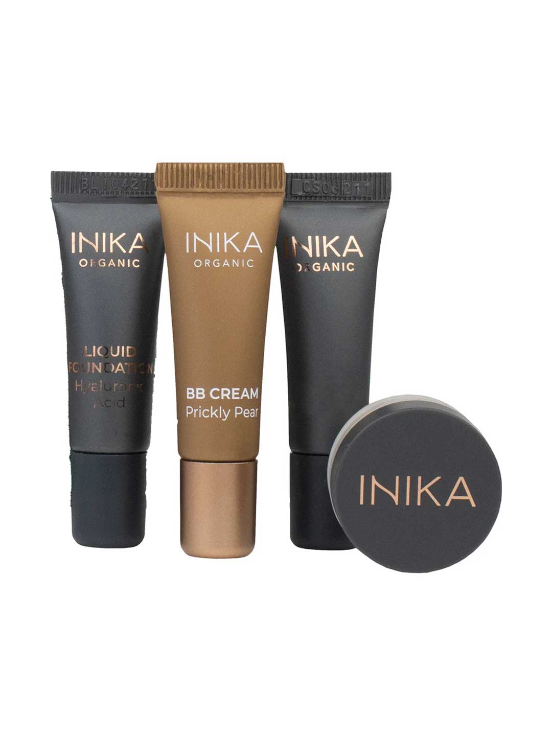 Four INIKA Organic Foundation Trial Sets - 4 Piece Set, featuring two black tubes, a bronze BB Cream Prickly Pear tube, and a small round black container, are displayed upright against a white background.