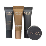 Four INIKA Organic Foundation Trial Sets - 4 Piece Set, featuring two black tubes, a bronze BB Cream Prickly Pear tube, and a small round black container, are displayed upright against a white background.