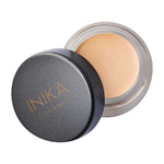 An open container of INIKA Organic Full Coverage Concealer 3.5g with a black lid beside it, showing the beige cream inside.