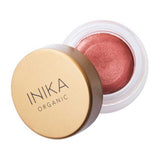 A small round jar of INIKA Organic Lip & Cheek Cream Petals 3.5g with a gold lid, slightly open to show shimmery pink cream inside.