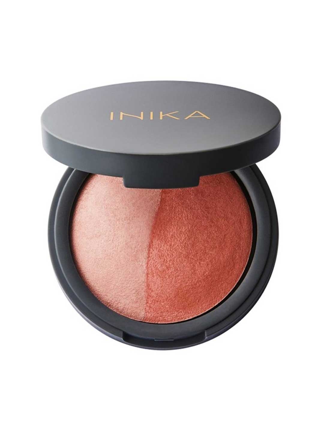 A round compact with a partially open black lid shows the INIKA name in gold. Inside is the INIKA Organic Mineral Baked Blush Duo - Burnt Peach 6.5g, a vegan blush featuring dome-shaped peach and bronze shades.