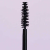 A close-up of the INIKA Organic Purity Lash Mascara - Black 8.5ml wand with bristles, standing upright against a light purple background—ideal for sensitive eyes and hypoallergenic needs.