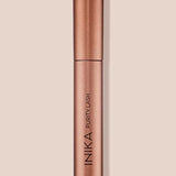 The INIKA Organic Purity Lash Mascara - Black 8.5ml stands upright in its metallic rose gold tube against a light beige background, with the brand and product name printed vertically—ideal for sensitive eyes.