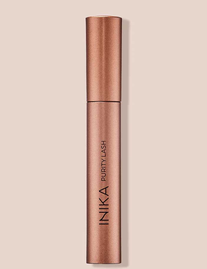 The INIKA Organic Purity Lash Mascara - Black 8.5ml stands upright in its metallic rose gold tube against a light beige background, with the brand and product name printed vertically—ideal for sensitive eyes.