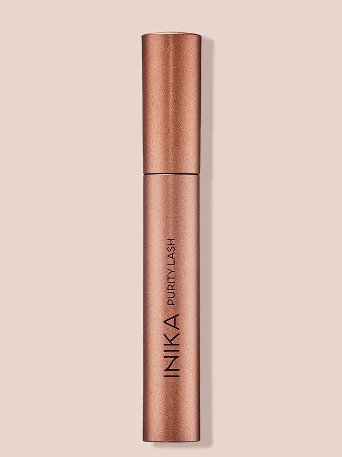 The INIKA Organic Purity Lash Mascara - Black 8.5ml stands upright in its metallic rose gold tube against a light beige background, with the brand and product name printed vertically—ideal for sensitive eyes.