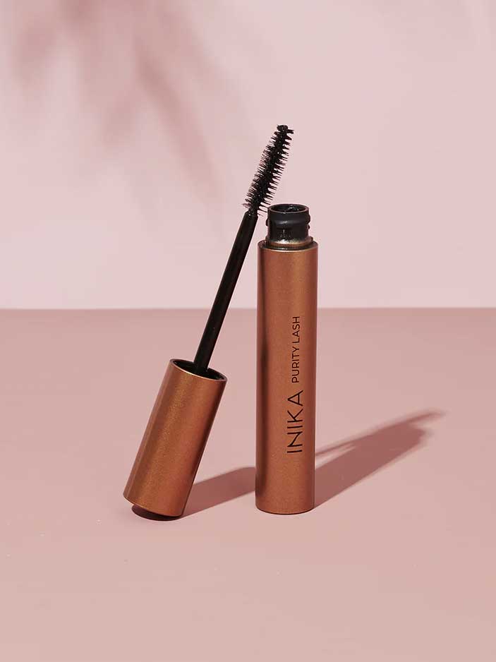 A black tube of INIKA Organic Purity Lash Mascara (8.5ml), hypoallergenic and ideal for sensitive eyes, with the wand resting on the open tube, set against a pale pink background.