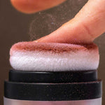 A finger presses onto the soft applicator of INIKA Organic Mineral Blush Puff Pot - Rosy Glow 3g, releasing a fine pink dust.