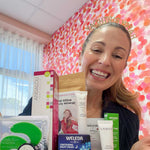 A smiling woman with light brown hair holds Clean Nectarine’s My Birthday Box—SOLD OUT—in front of a colorful pink polka-dot background. The limited edition box features skincare creams, mascara, and tint from various brands.