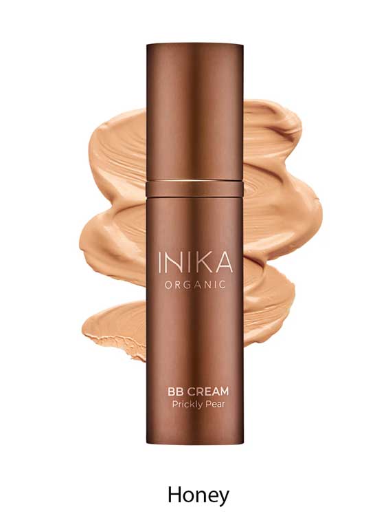 A bottle of INIKA Organic Organic BB Cream 30ml in the shade Honey, a vegan beauty balm, is displayed in front of a creamy tan swatch showcasing its natural satin finish.