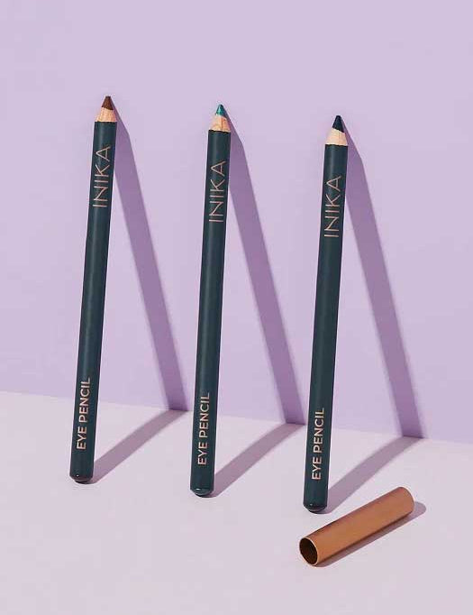 Three INIKA Organic Eye Liner Pencils (9.9g) stand upright on a light purple surface, each showcasing a unique tip color. A gold cap rests beside them—ideal for sensitive eyes seeking gentle definition.